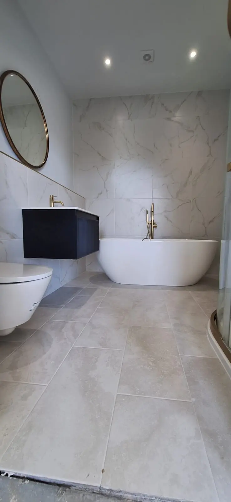 A finished marble bathroom with a freestanding bath and gold taps