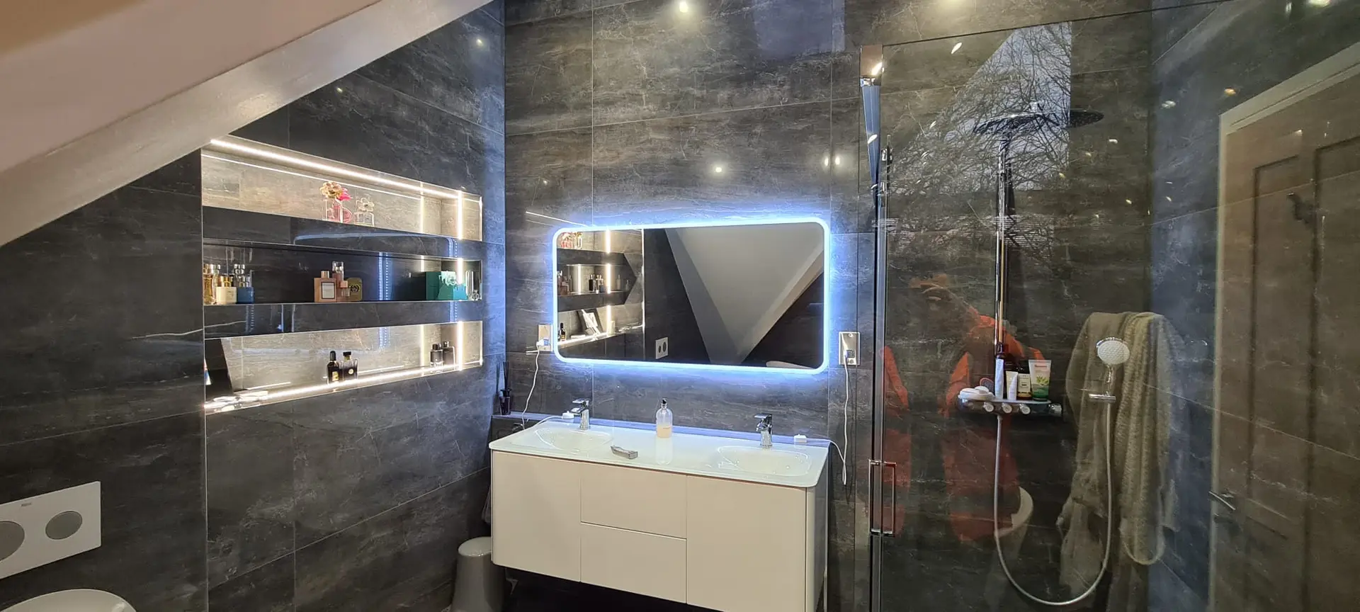 A luxury stone bathroom with backlit shelving and walk-in shower